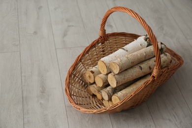 Photo of Wicker basket with firewood on floor indoors, space for text