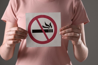 Photo of Woman holding card with no smoking sign on gray background, closeup