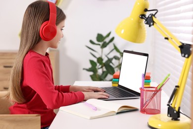 Photo of E-learning. Girl using laptop and headphones during online lesson at table indoors