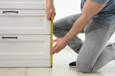 Photo of Man measuring chest of drawers indoors, closeup. Construction tool