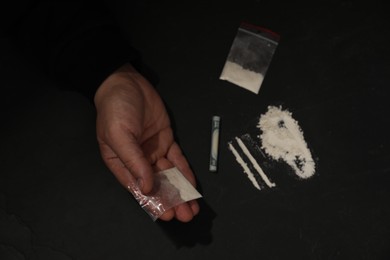 Photo of Drug addiction. Man with cocaine and rolled dollar banknote at dark table, top view