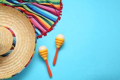 Photo of Mexican sombrero hat, maracas and colorful poncho on light blue background, flat lay. Space for text