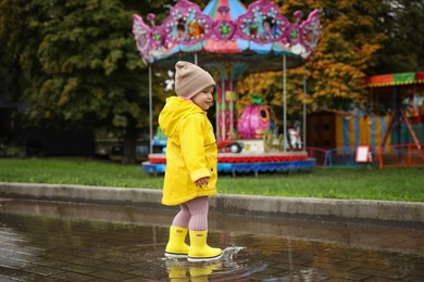 Photo of Cute little girl standing in puddle near carousel outdoors