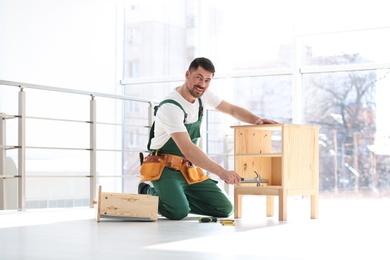 Photo of Handyman in uniform assembling furniture indoors. Professional construction tools