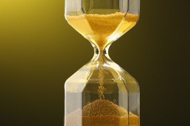 Photo of Hourglass with golden flowing sand on color background, closeup