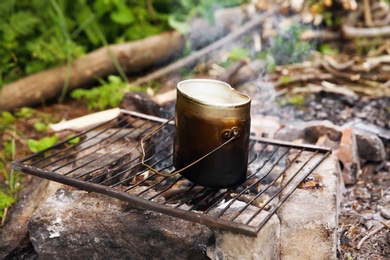 Photo of Cooking food on rack over bonfire in wilderness