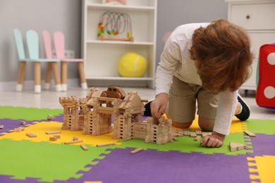 Photo of Little boy playing with wooden construction set on puzzle mat in room. Child's toy