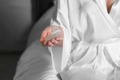 Photo of Woman holding unrolled condom on bed, closeup. Safe sex