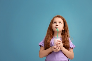 Little girl with glass of delicious milk shake on color background