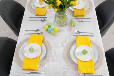 Photo of Festive table setting with glasses, painted eggs and vase of tulips, view from above. Easter celebration