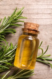 Bottle of essential oil and fresh rosemary on wooden table, flat lay