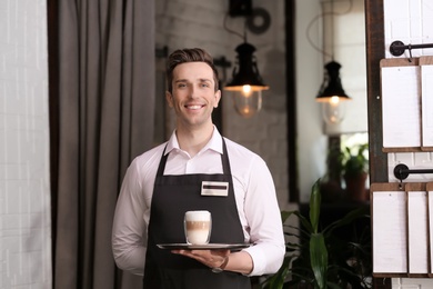 Photo of Young waiter holding tray with glass of coffee at workplace
