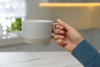 Photo of Woman holding elegant cup in kitchen, closeup
