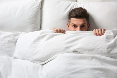 Photo of Handsome man covering his face with blanket while lying in bed at home