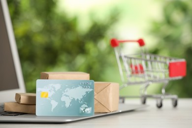 Photo of Online payment concept. Bank card and small boxes with laptop on white table