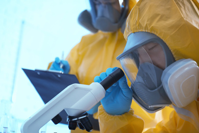 Photo of Scientist in chemical protective suit using microscope at laboratory, closeup. Virus research