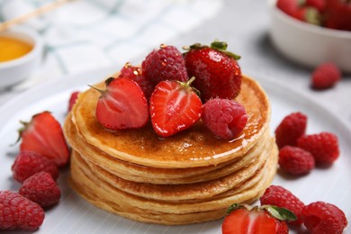 Photo of Tasty pancakes with fresh berries and honey on plate, closeup