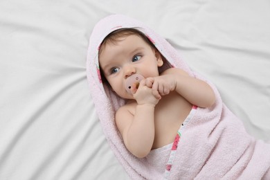 Photo of Cute little baby with pacifier in hooded towel after bathing on bed, top view