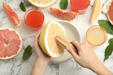 Photo of Woman squeezing pomelo juice with reamer at white marble table, top view