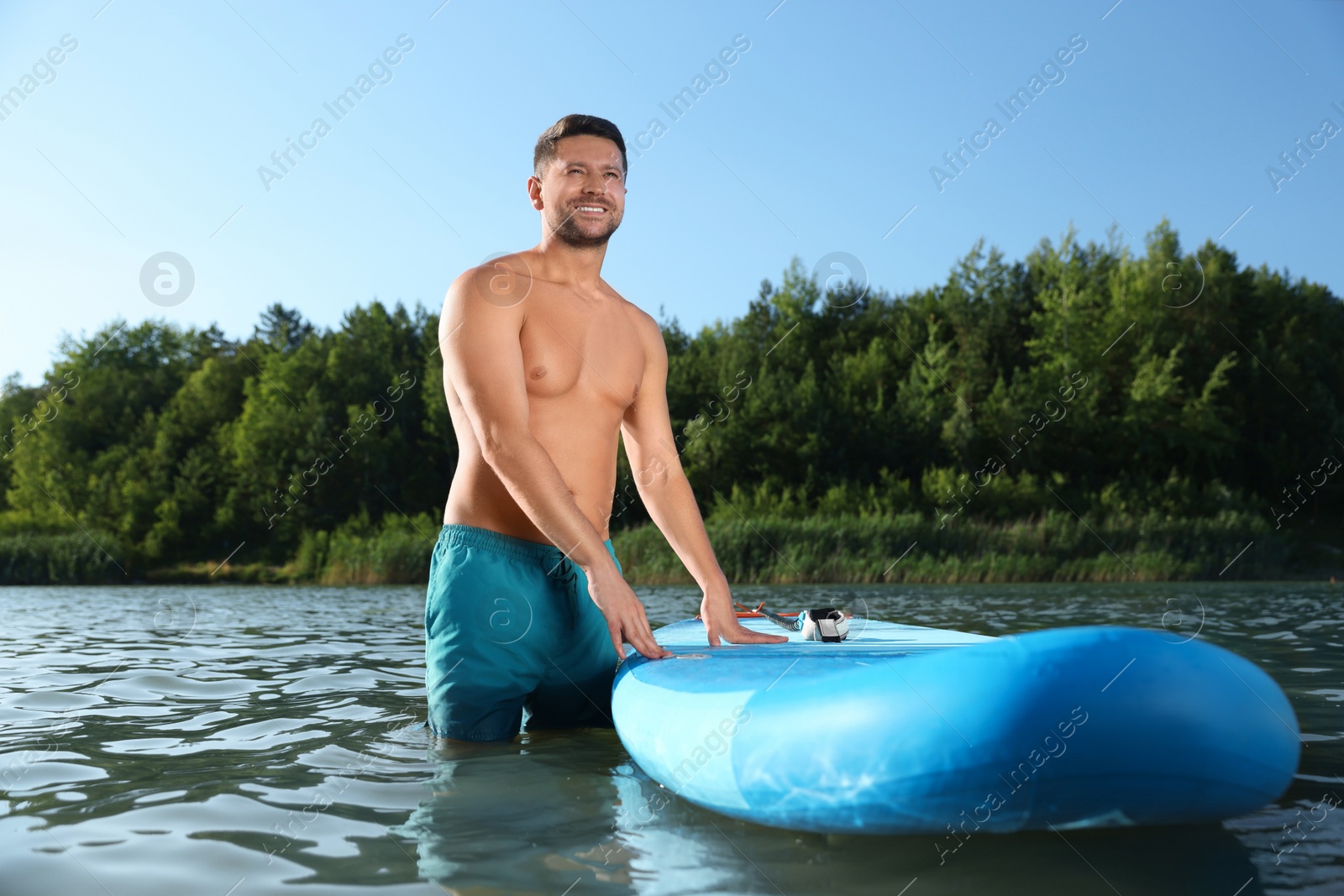 Photo of Man standing near SUP board in river water on sunny day