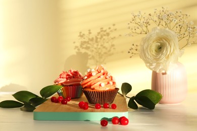 Photo of Delicious cupcake with bright cream and flowers on white wooden table