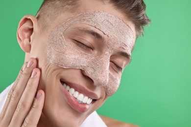 Photo of Handsome man applying facial mask onto his face on green background, closeup