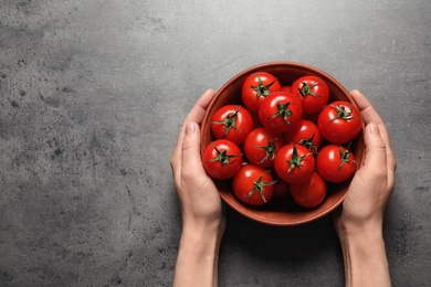 Photo of Woman holding wooden bowl with ripe cherry tomatoes at table, above view. Space for text