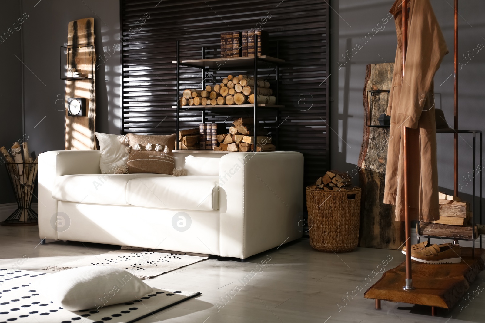 Photo of Shelving unit with stacked firewood and comfortable sofa in stylish room interior