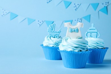 Photo of Beautifully decorated baby shower cupcakes with cream and boy toppers on light blue background. Space for text