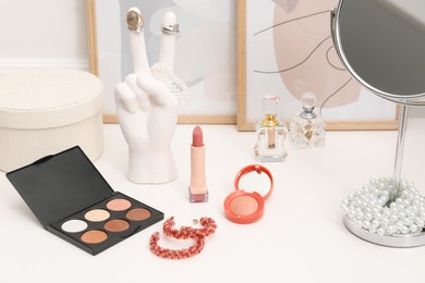 Photo of Mirror, cosmetic products, perfumes and jewelry on white dressing table, closeup