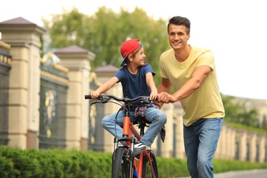 Image of Dad teaching son to ride bicycle outdoors