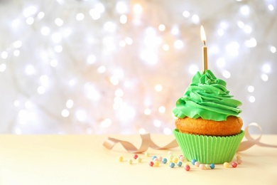 Photo of Delicious birthday cupcake with candle on table against blurred background