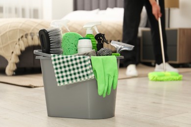 Photo of Woman cleaning floor, focus on different supplies in bucket at home