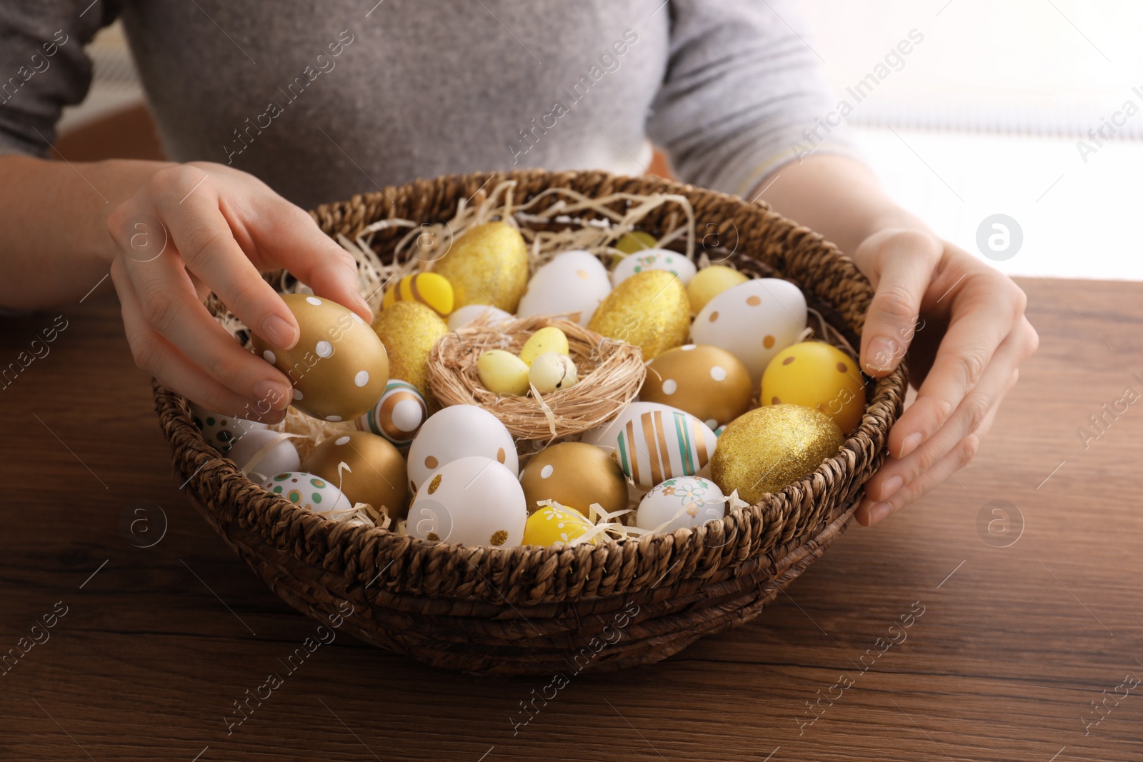 Woman with basket full of dyed Easter eggs at wooden table, closeup. Easter celebration Photo of Woman with basket full of dyed Easter eggs at wooden table, closeup. Easter celebration