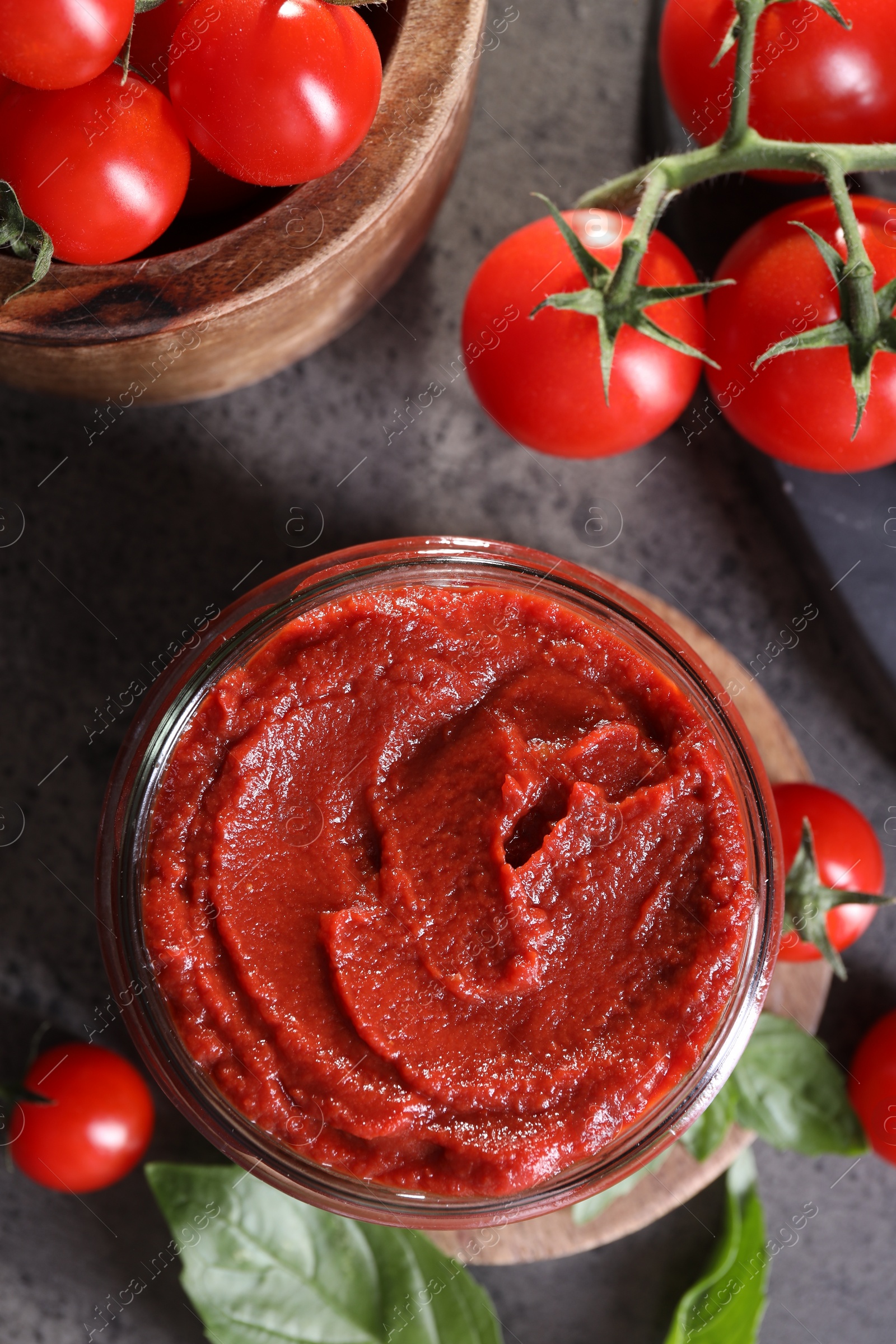 Photo of Jar of tasty tomato paste and ingredients on grey textured table, flat lay