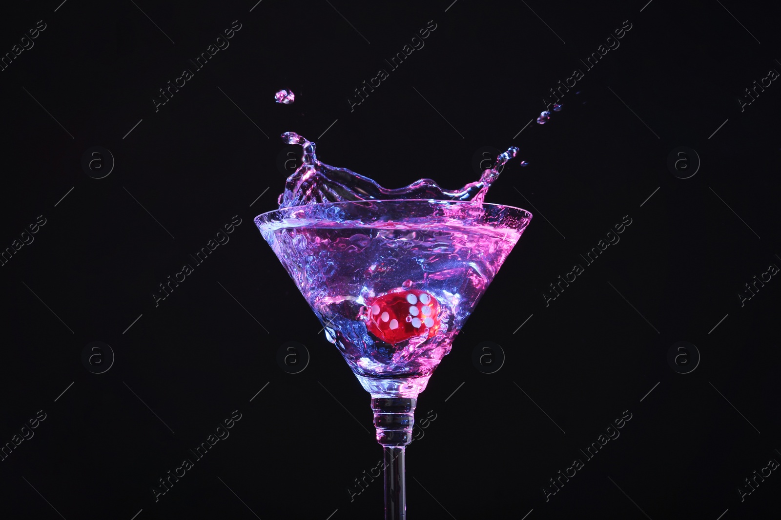 Photo of Casino dice falling into glass of alcohol drink on black background