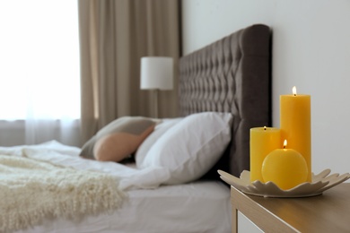 Photo of Burning candles on bedside table in bedroom