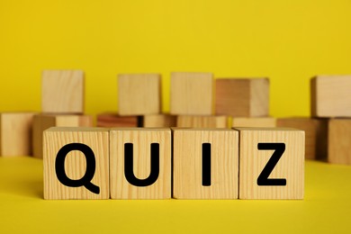 Photo of Wooden cubes with word Quiz on yellow background. Space for text
