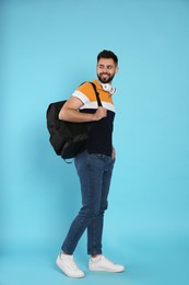 Photo of Young man with stylish backpack and headphones on light blue background