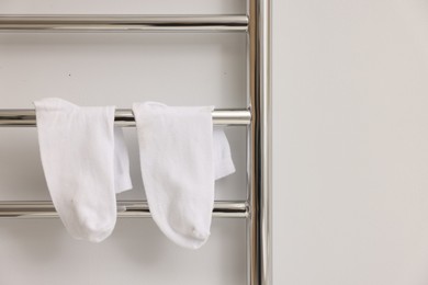 Photo of Heated towel rail with socks on white wall, closeup. Space for text