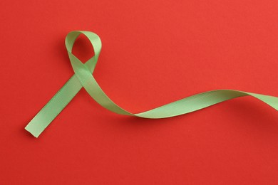 Photo of Light green awareness ribbon on red background, top view