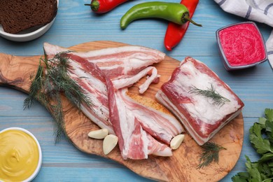 Photo of Pieces of pork fatback with garlic and dill on light blue wooden table, flat lay