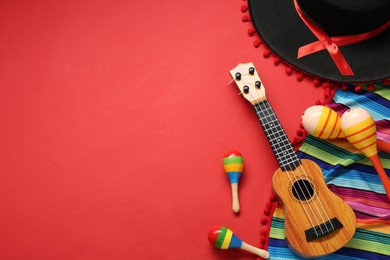 Photo of Mexican sombrero hat, maracas, guitar and colorful poncho on red background, flat lay. Space for text
