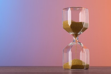 Photo of Hourglass with flowing sand on table against color background, space for text