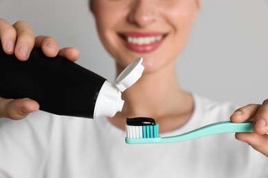 Photo of Woman applying charcoal toothpaste onto brush on grey background, closeup