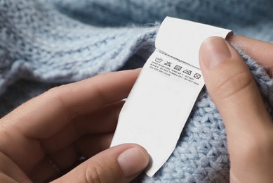 Photo of Woman holding clothing label on light blue garment, closeup