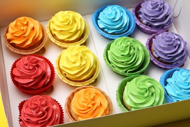 Photo of Many tasty cupcakes with colorful cream in box, closeup