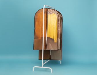 Photo of Garment bags with clothes on rack against light blue background. Space for text