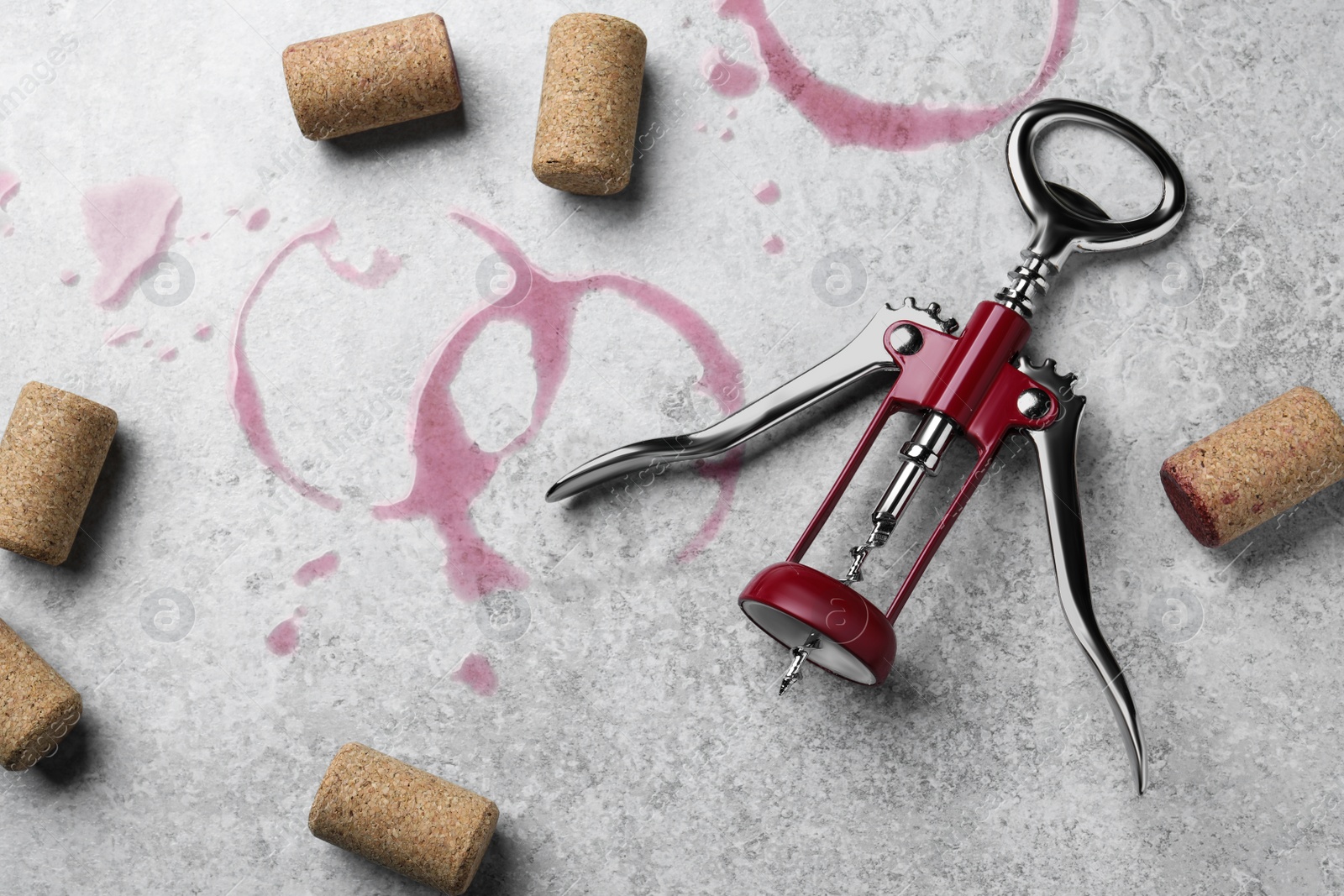 Photo of Wine stains, corkscrew and stoppers on light grey stone table, flat lay