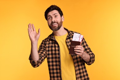 Photo of Smiling man with passport and tickets waving hello on yellow background